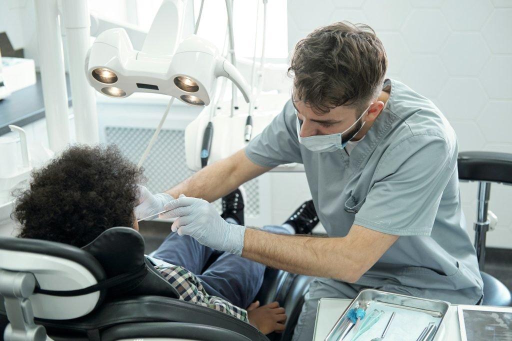 Dentist bending over little boy while drilling his tooth