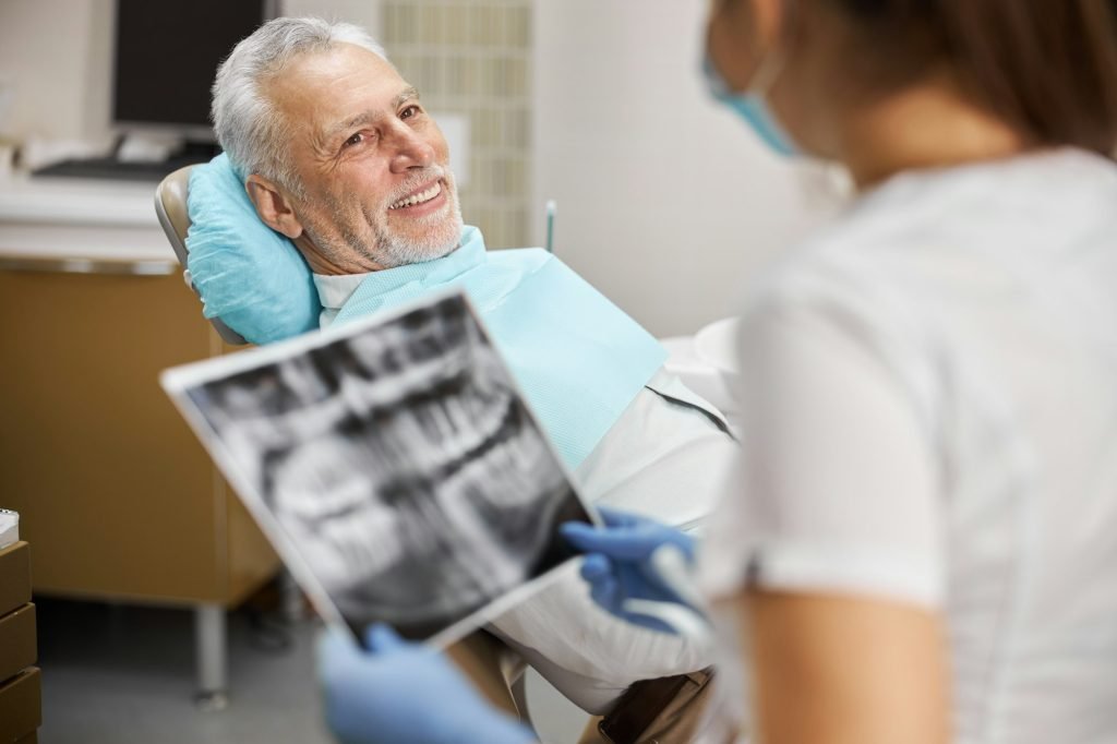 Senior citizen sitting in dental chair looking at a dental technician