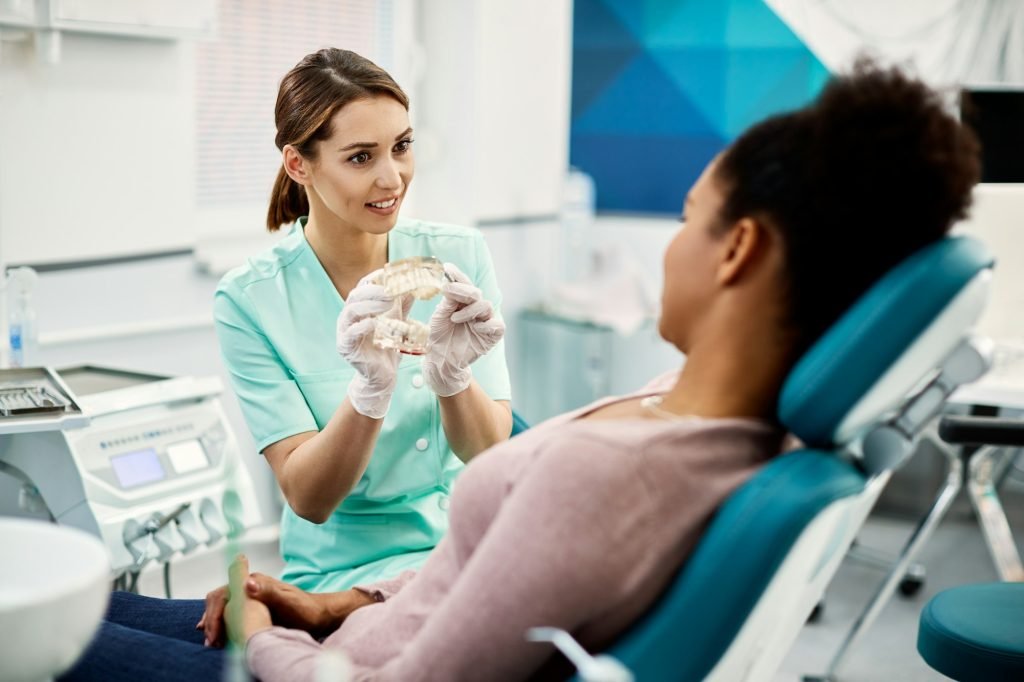 Young orthodontist talking about dental prosthetic with her patient at dentist's office.